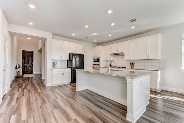 kitchen with a center island with sink, light wood finished floors, stainless steel appliances, visible vents, and under cabinet range hood