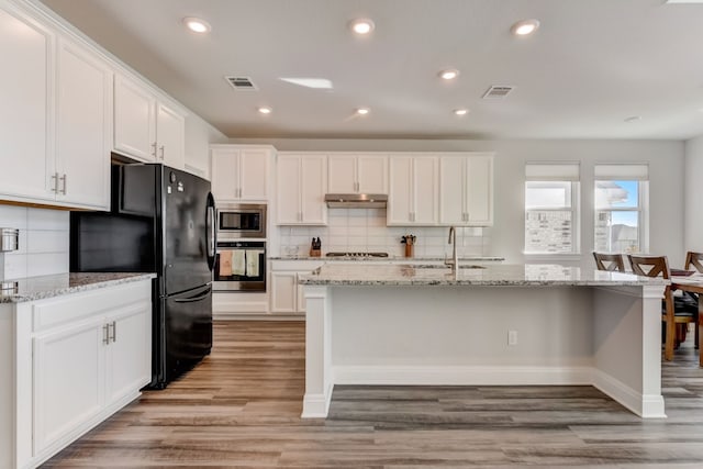 kitchen with white cabinets, appliances with stainless steel finishes, a sink, decorative backsplash, and under cabinet range hood