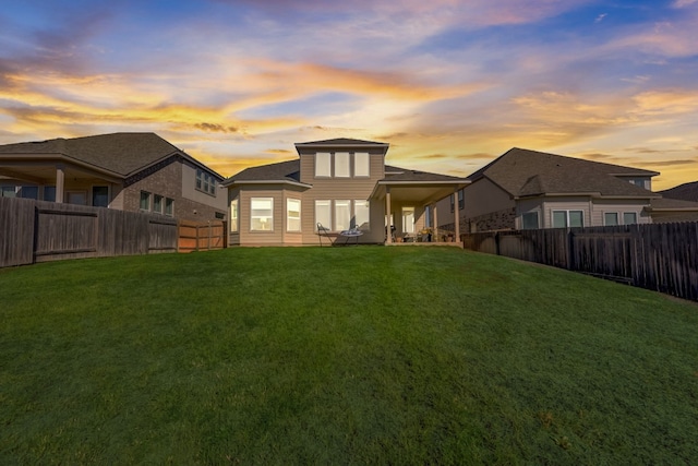 back of house at dusk with a fenced backyard and a yard