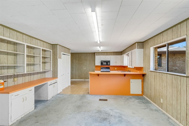 kitchen featuring built in desk, wooden walls, and white cabinetry