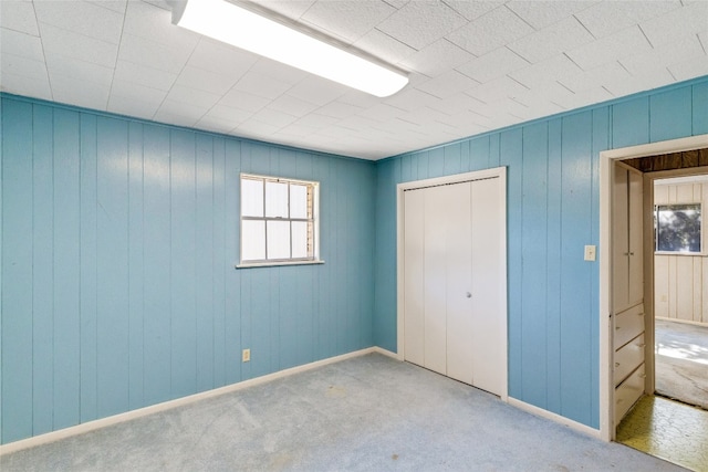 unfurnished bedroom with multiple windows, wood walls, a closet, and carpet flooring