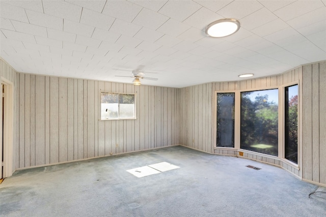 empty room with ceiling fan, wood walls, and carpet floors