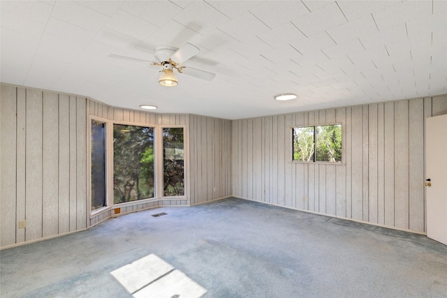 carpeted empty room featuring ceiling fan and wood walls