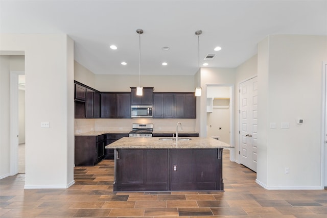 kitchen featuring pendant lighting, a kitchen island with sink, appliances with stainless steel finishes, sink, and dark brown cabinets