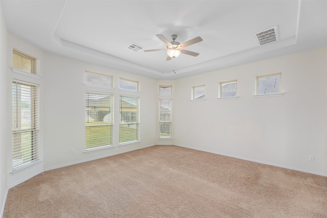 spare room with ceiling fan, a raised ceiling, and light carpet