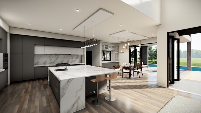kitchen with a sink, a center island with sink, modern cabinets, wood finished floors, and pendant lighting