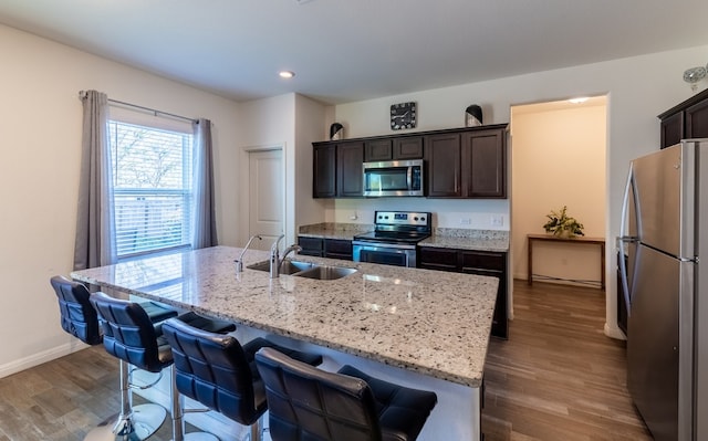 kitchen featuring light stone countertops, stainless steel appliances, sink, a center island with sink, and hardwood / wood-style floors