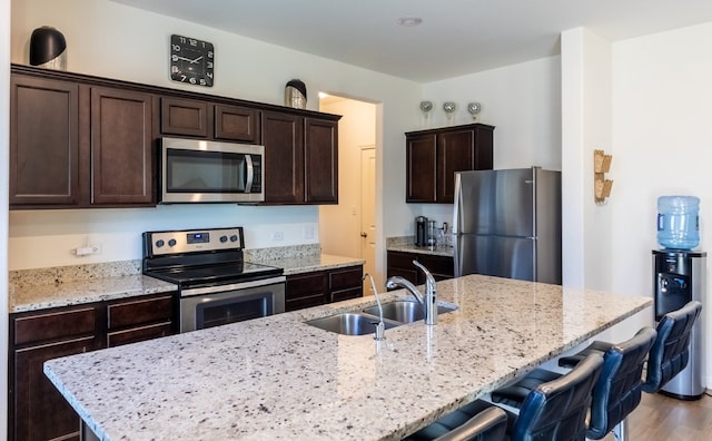 kitchen with appliances with stainless steel finishes, sink, light stone counters, and wood-type flooring