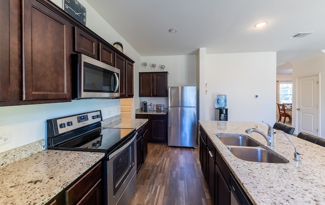 kitchen with sink, dark hardwood / wood-style floors, appliances with stainless steel finishes, dark brown cabinets, and light stone counters