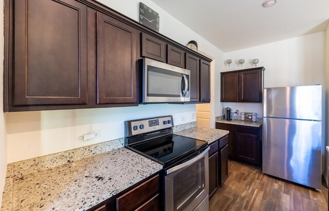 kitchen with light stone countertops, appliances with stainless steel finishes, dark brown cabinetry, and dark wood-type flooring