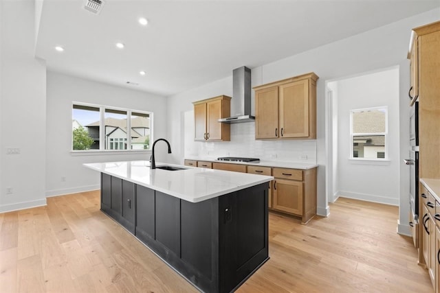 kitchen featuring a center island with sink, wall chimney exhaust hood, gas stovetop, and light wood-type flooring