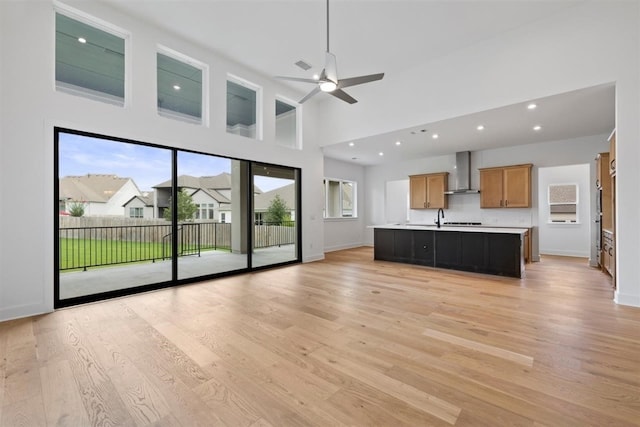 unfurnished living room featuring ceiling fan, plenty of natural light, light hardwood / wood-style floors, and a high ceiling