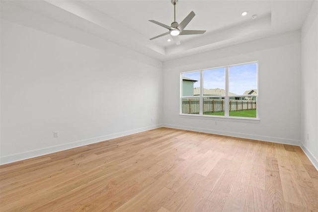 unfurnished room featuring ceiling fan, light hardwood / wood-style flooring, and a tray ceiling