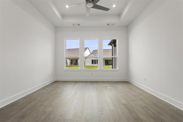 unfurnished room featuring ceiling fan, wood-type flooring, and a raised ceiling