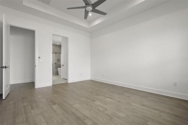 unfurnished bedroom featuring hardwood / wood-style flooring, ceiling fan, ensuite bath, and a raised ceiling