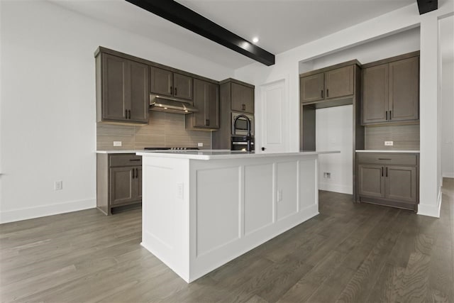 kitchen with tasteful backsplash, beam ceiling, dark hardwood / wood-style floors, and a kitchen island with sink