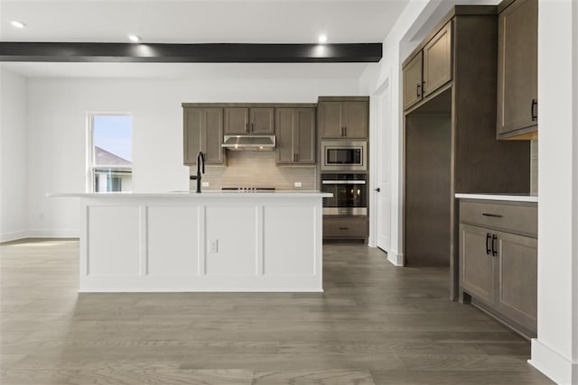 kitchen featuring beamed ceiling, hardwood / wood-style floors, an island with sink, and stainless steel appliances