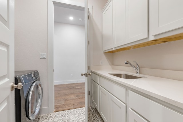 washroom featuring a sink, baseboards, light wood-type flooring, cabinet space, and washer / clothes dryer