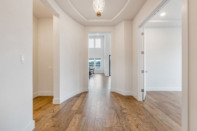 hallway with light wood-type flooring, a raised ceiling, and baseboards