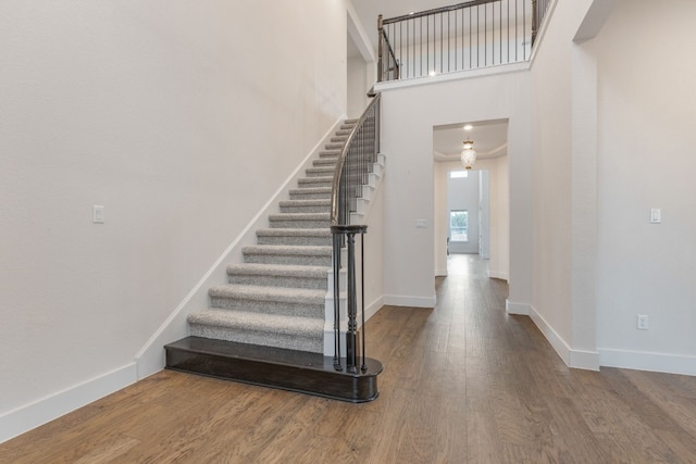 stairs featuring a high ceiling, baseboards, and wood finished floors