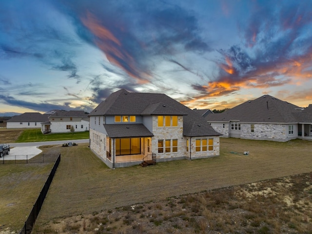 rear view of property featuring stone siding, a yard, and fence