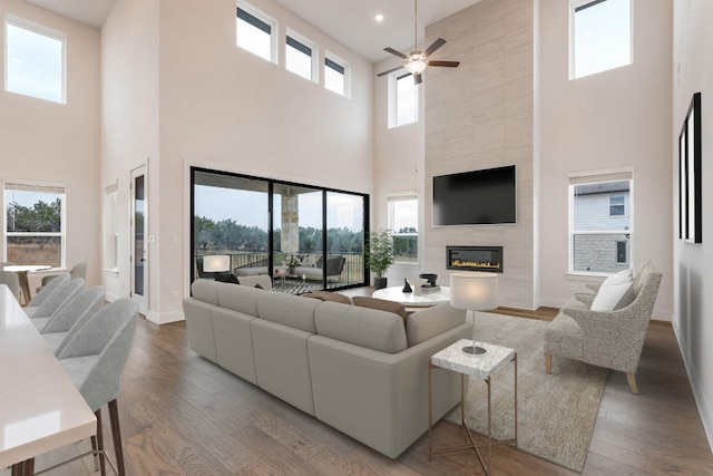 living room featuring a fireplace, ceiling fan, hardwood / wood-style flooring, and a towering ceiling