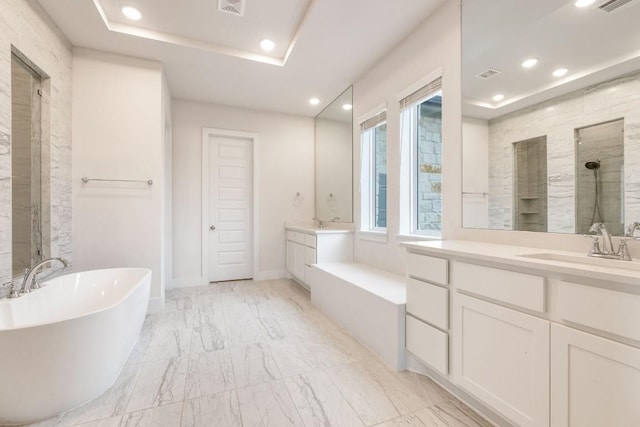 bathroom with a tray ceiling, two vanities, a freestanding tub, and recessed lighting