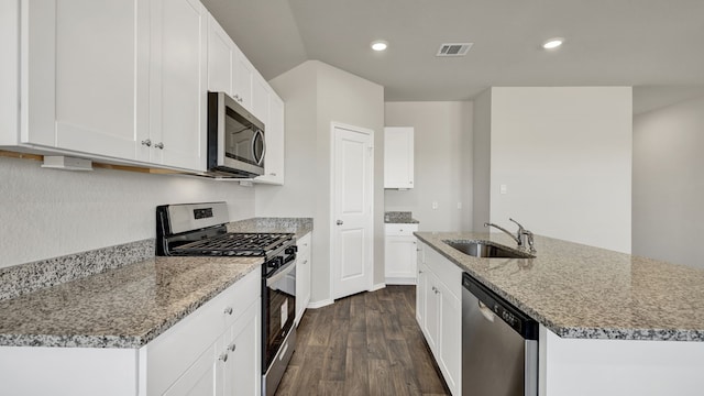 kitchen with stainless steel appliances, an island with sink, light stone countertops, sink, and white cabinetry