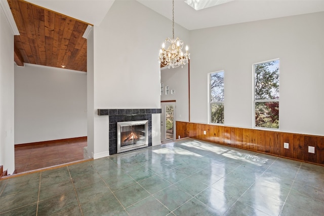 unfurnished living room featuring wooden ceiling, high vaulted ceiling, a tile fireplace, wooden walls, and a chandelier