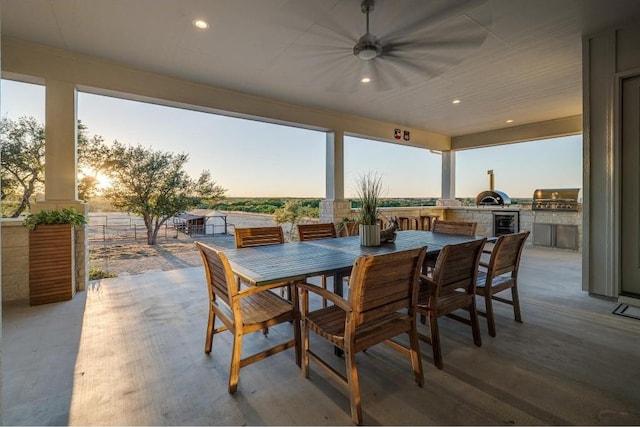 patio terrace at dusk featuring area for grilling, ceiling fan, and exterior kitchen