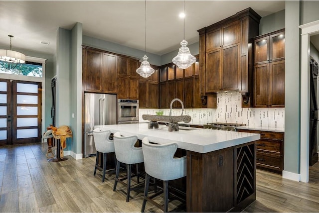 kitchen with stainless steel appliances, hanging light fixtures, a center island with sink, and sink