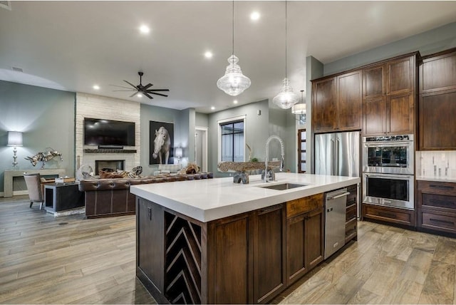 kitchen featuring dark brown cabinetry, sink, hanging light fixtures, a kitchen island with sink, and appliances with stainless steel finishes