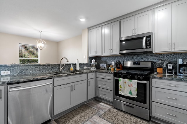 kitchen featuring appliances with stainless steel finishes, gray cabinetry, dark stone countertops, and sink