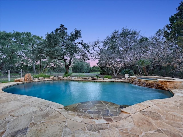 pool at dusk with an in ground hot tub and a patio