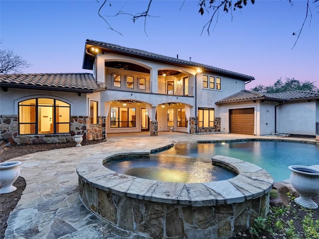 back house at dusk with ceiling fan, a balcony, a swimming pool with hot tub, and a patio