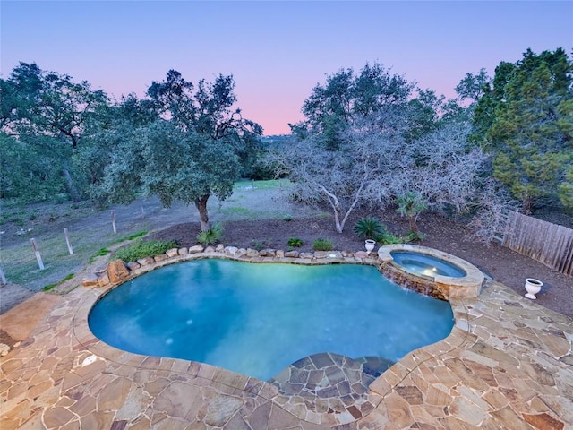 pool at dusk with a patio area and an in ground hot tub