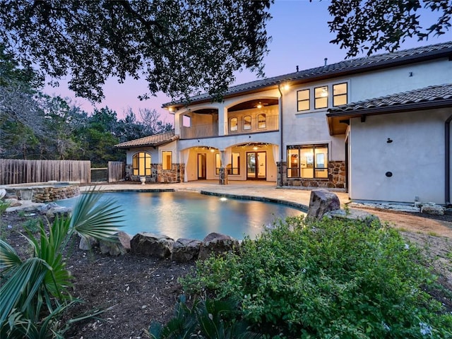 back house at dusk with a swimming pool with hot tub, a patio area, and a balcony