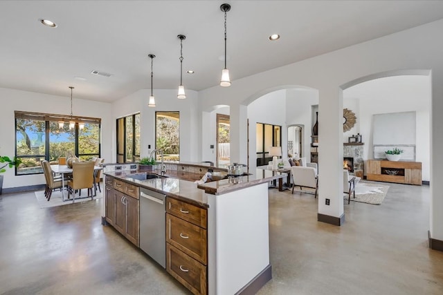 kitchen featuring sink, hanging light fixtures, a kitchen island with sink, stainless steel dishwasher, and light stone countertops