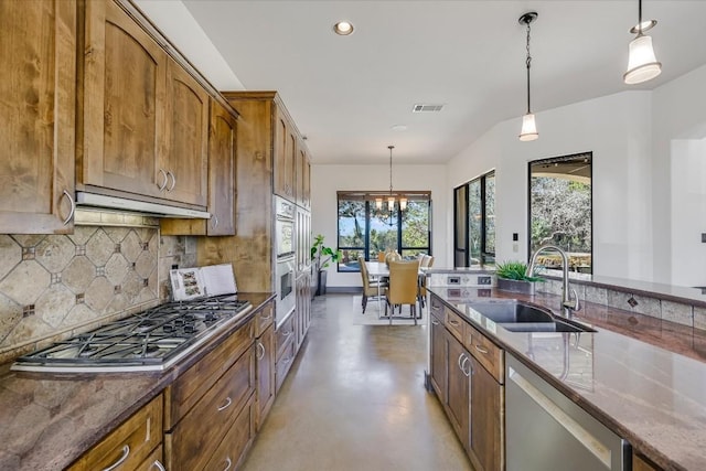 kitchen featuring stainless steel appliances, sink, decorative light fixtures, and dark stone counters