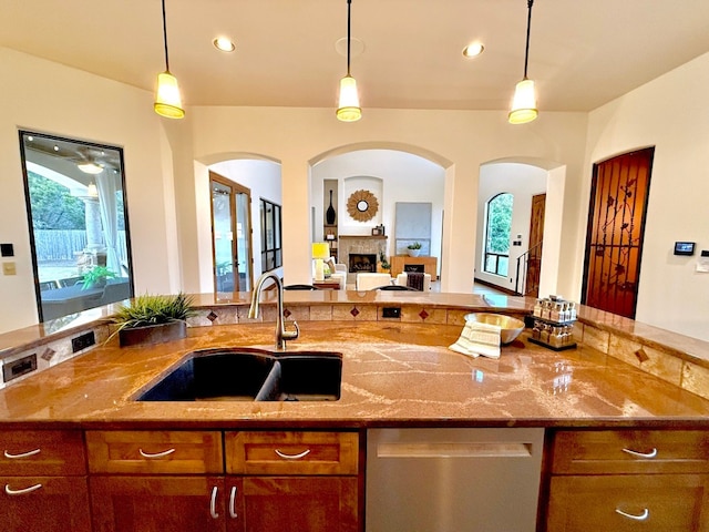 kitchen with sink, stainless steel dishwasher, hanging light fixtures, and light stone countertops