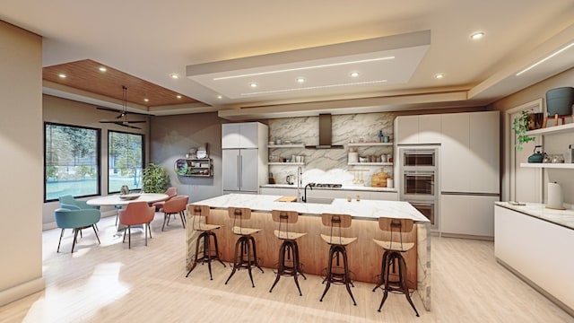 kitchen featuring stainless steel appliances, a kitchen bar, an island with sink, and wall chimney range hood