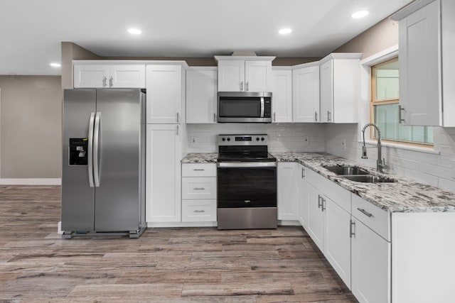 kitchen featuring appliances with stainless steel finishes, backsplash, sink, white cabinets, and wood-type flooring