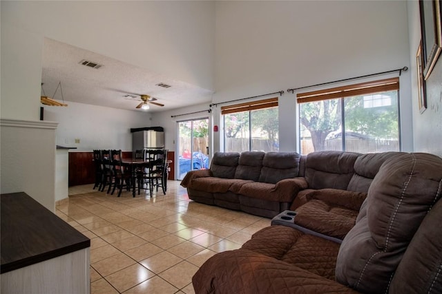 living room with visible vents, light tile patterned flooring, ceiling fan, a towering ceiling, and a textured ceiling