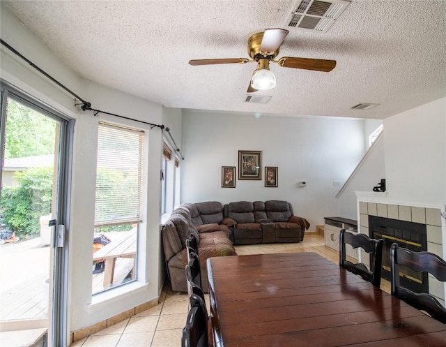 dining space with visible vents, ceiling fan, light tile patterned floors, a fireplace, and a textured ceiling