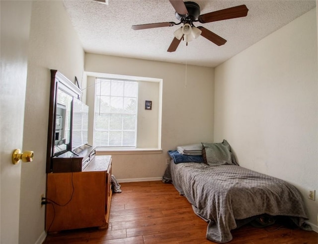 bedroom with ceiling fan, a textured ceiling, baseboards, and wood-type flooring