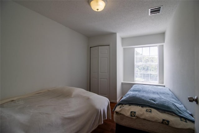 bedroom with dark wood-style floors, visible vents, a closet, and a textured ceiling