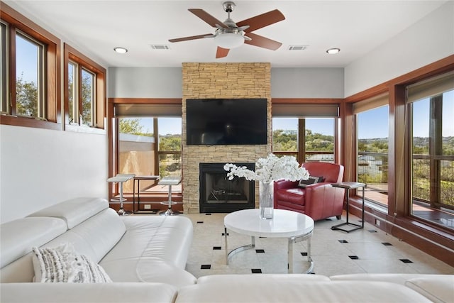 tiled living room featuring a stone fireplace, a wealth of natural light, and ceiling fan