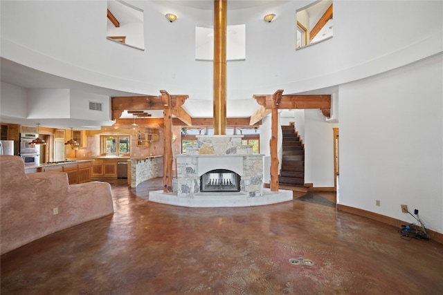 unfurnished living room with a towering ceiling, a stone fireplace, and concrete flooring