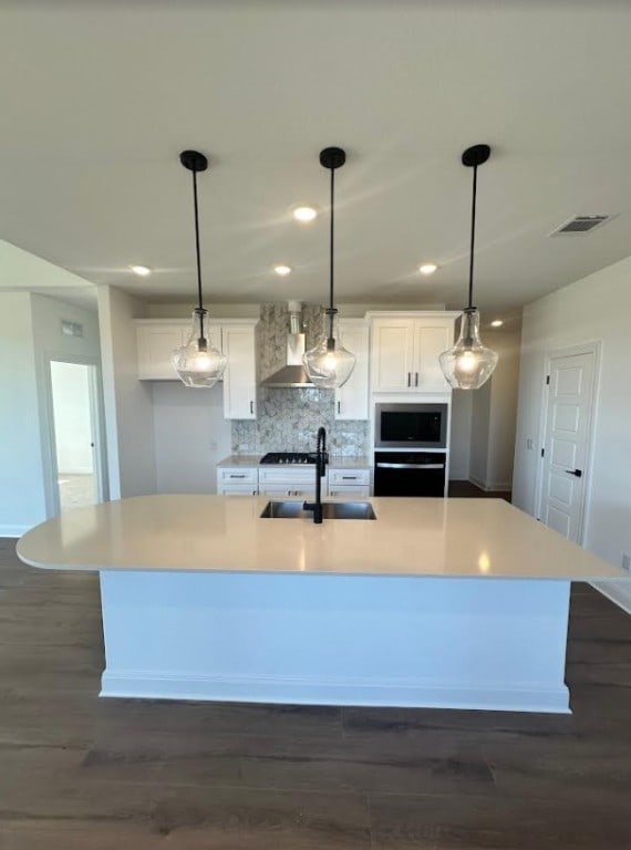 kitchen featuring an island with sink, appliances with stainless steel finishes, wall chimney range hood, and sink