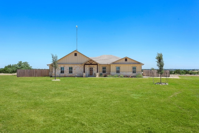 back of property featuring board and batten siding, stone siding, fence, and a lawn